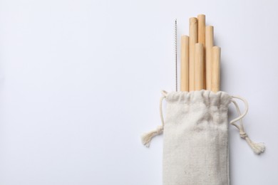 Photo of Bamboo drinking straws and cleaning brush in bag on white background, top view. Space for text