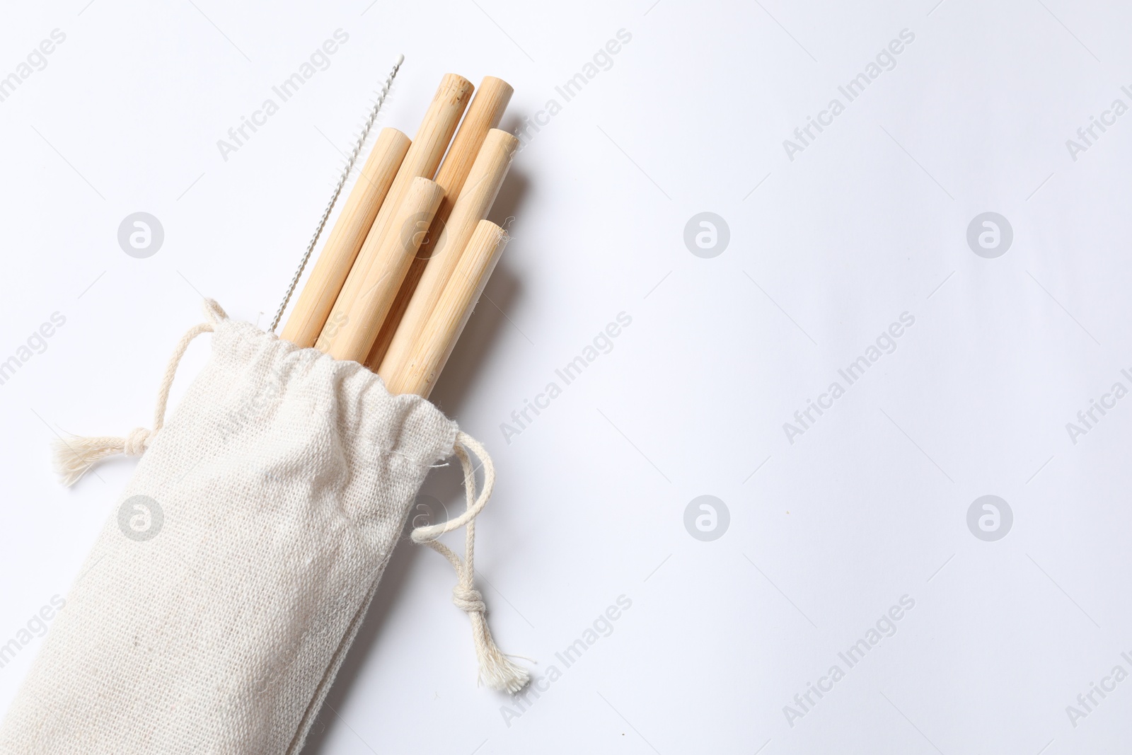 Photo of Bamboo drinking straws and cleaning brush in bag on white background, top view. Space for text