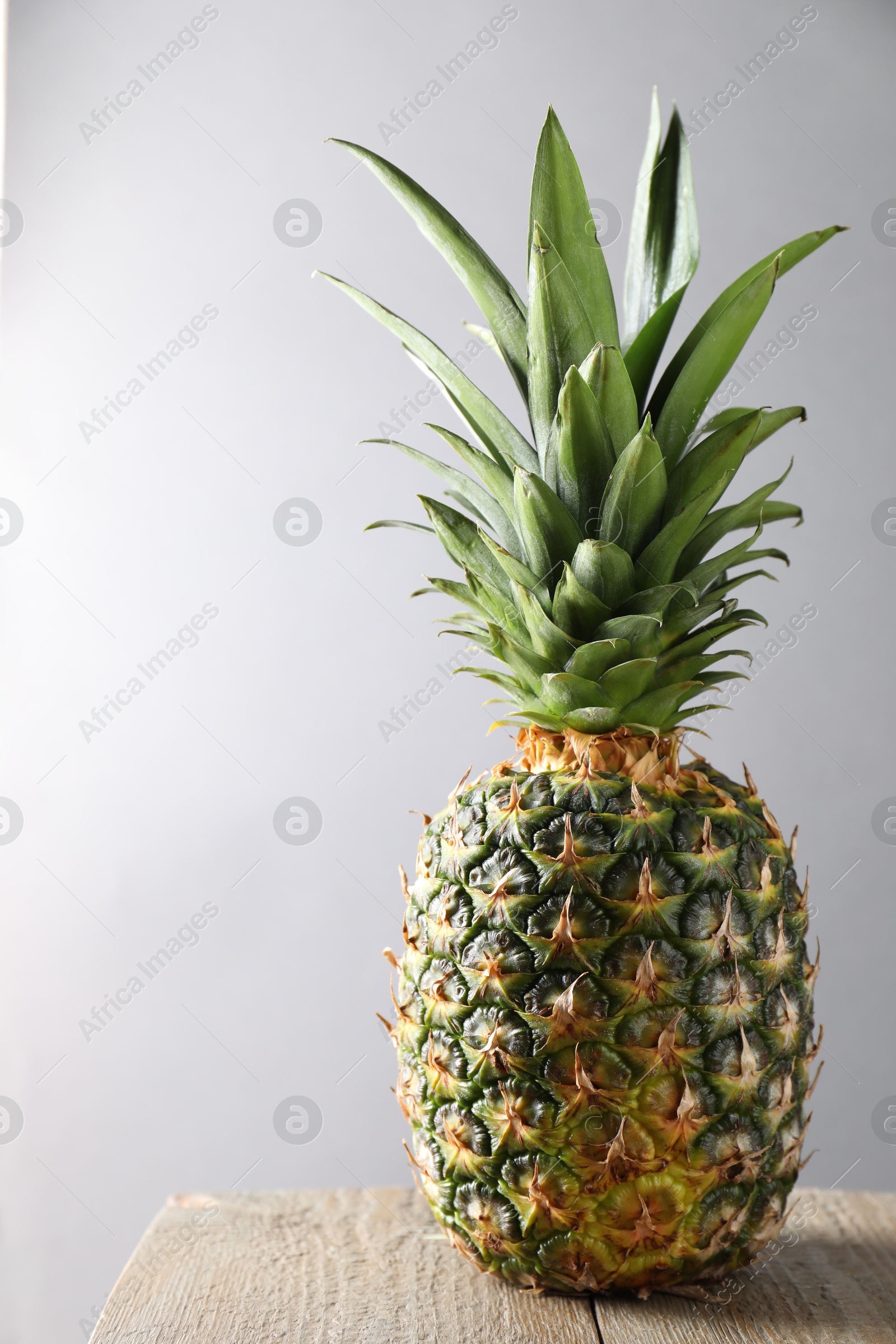 Photo of Fresh ripe pineapple on wooden table against light grey background