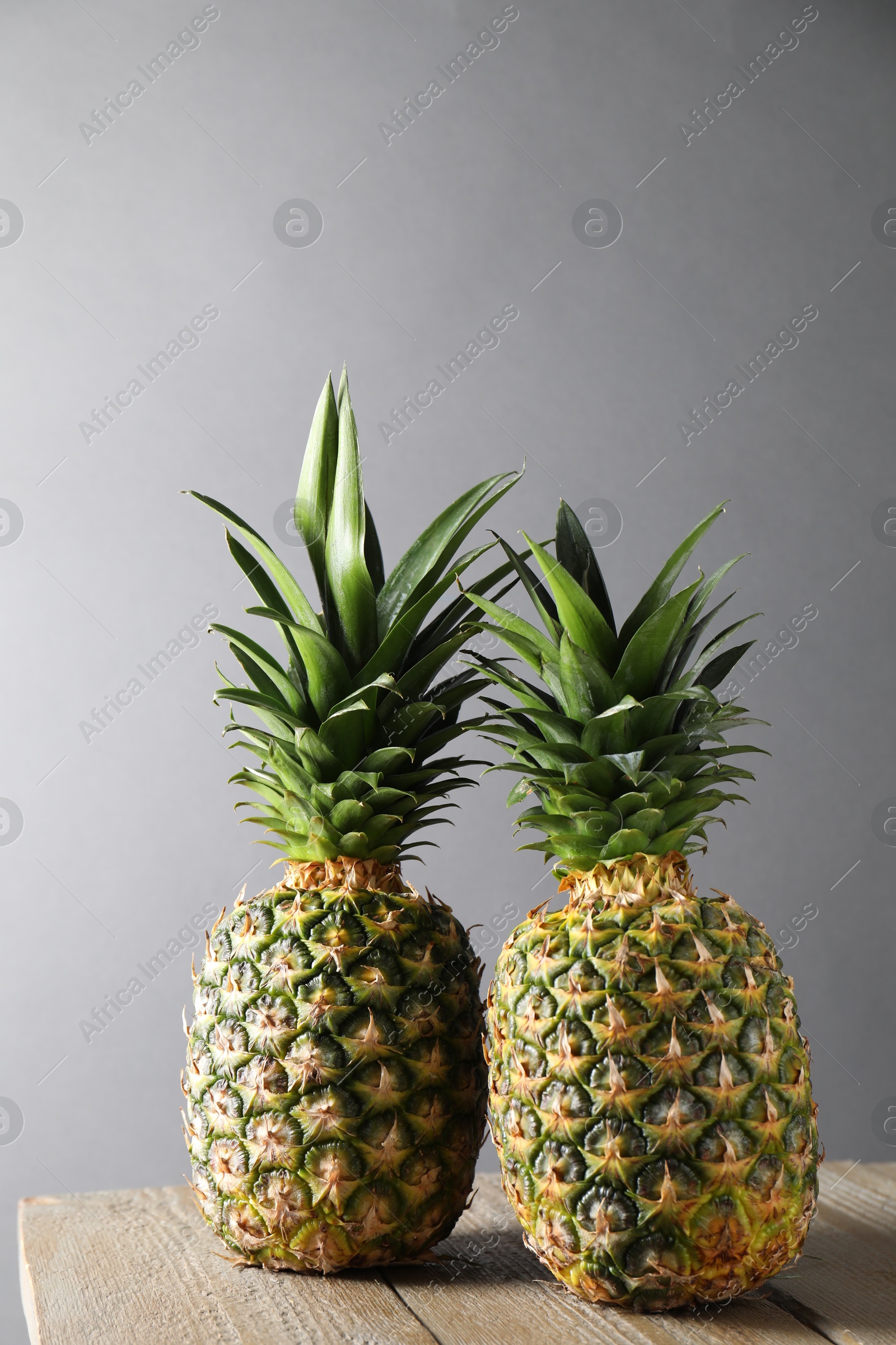 Photo of Fresh ripe pineapples on wooden table against light grey background