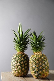 Fresh ripe pineapples on wooden table against light grey background