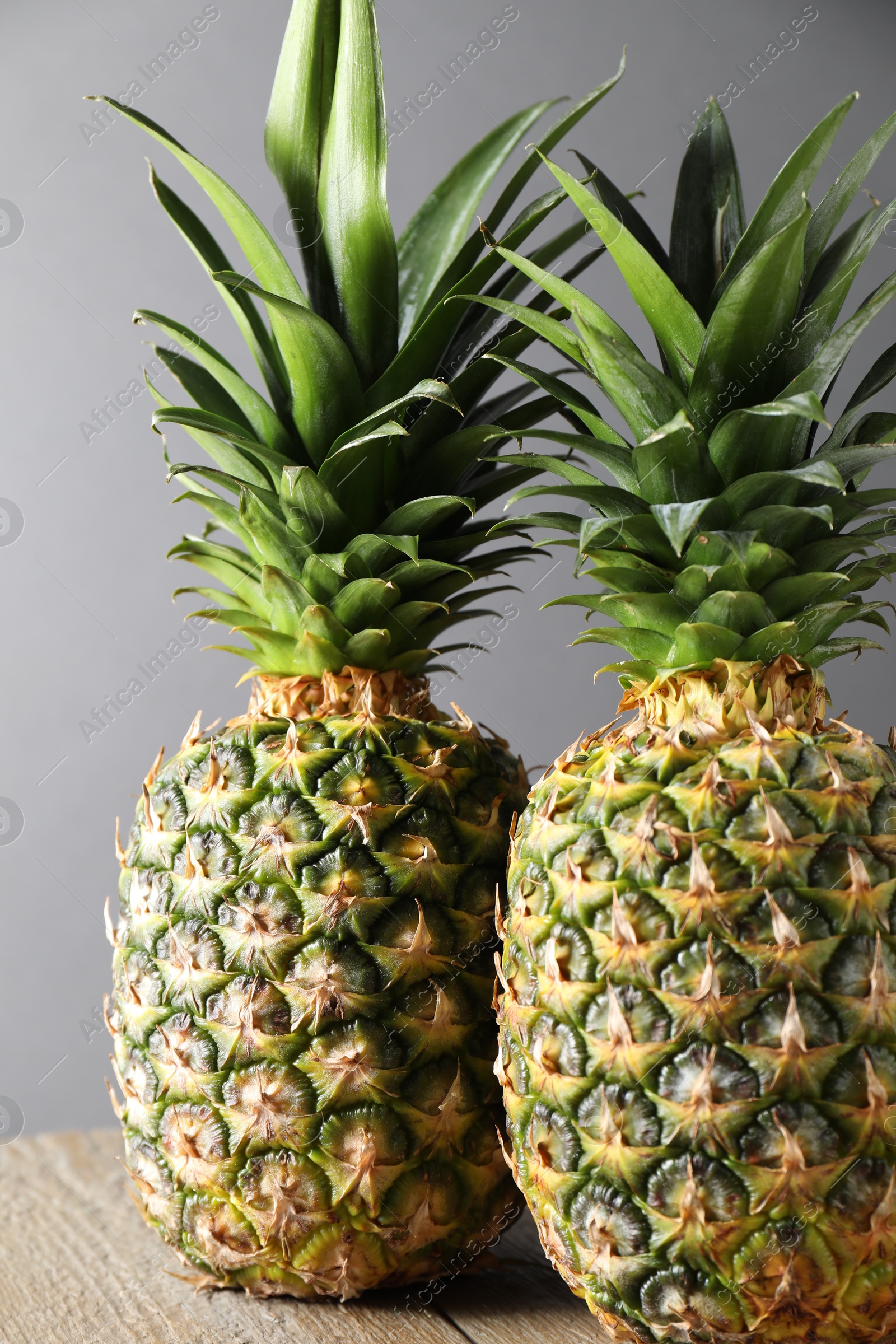 Photo of Fresh ripe pineapples on wooden table against light grey background, closeup