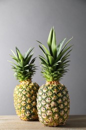 Photo of Fresh ripe pineapples on wooden table against light grey background