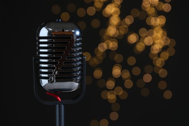 Photo of Sound recording and reinforcement. Vintage microphone against black background with blurred lights, closeup. Space for text