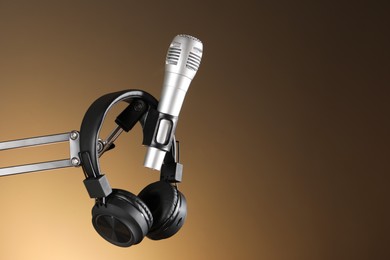 Photo of Stand with microphone and headphones on light brown background, space for text. Sound recording and reinforcement