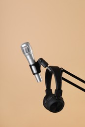 Photo of Stand with microphone and headphones on beige background. Sound recording and reinforcement