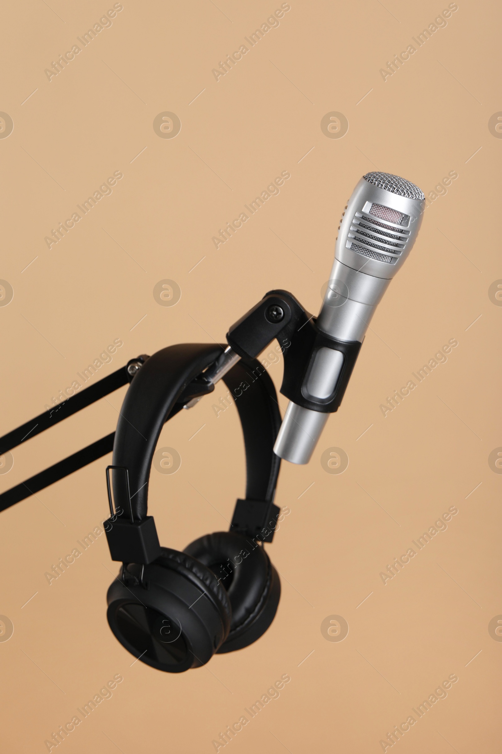 Photo of Stand with microphone and headphones on beige background. Sound recording and reinforcement