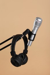 Photo of Stand with microphone and headphones on beige background. Sound recording and reinforcement