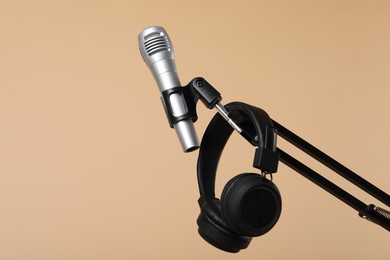 Photo of Stand with microphone and headphones on beige background, space for text. Sound recording and reinforcement