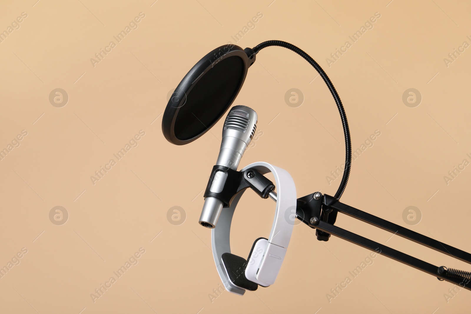 Photo of Stand with microphone, headphones and pop filter on beige background, space for text. Sound recording and reinforcement