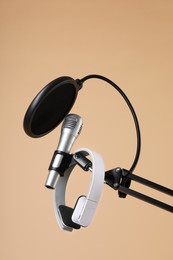 Photo of Stand with microphone, headphones and pop filter on beige background. Sound recording and reinforcement