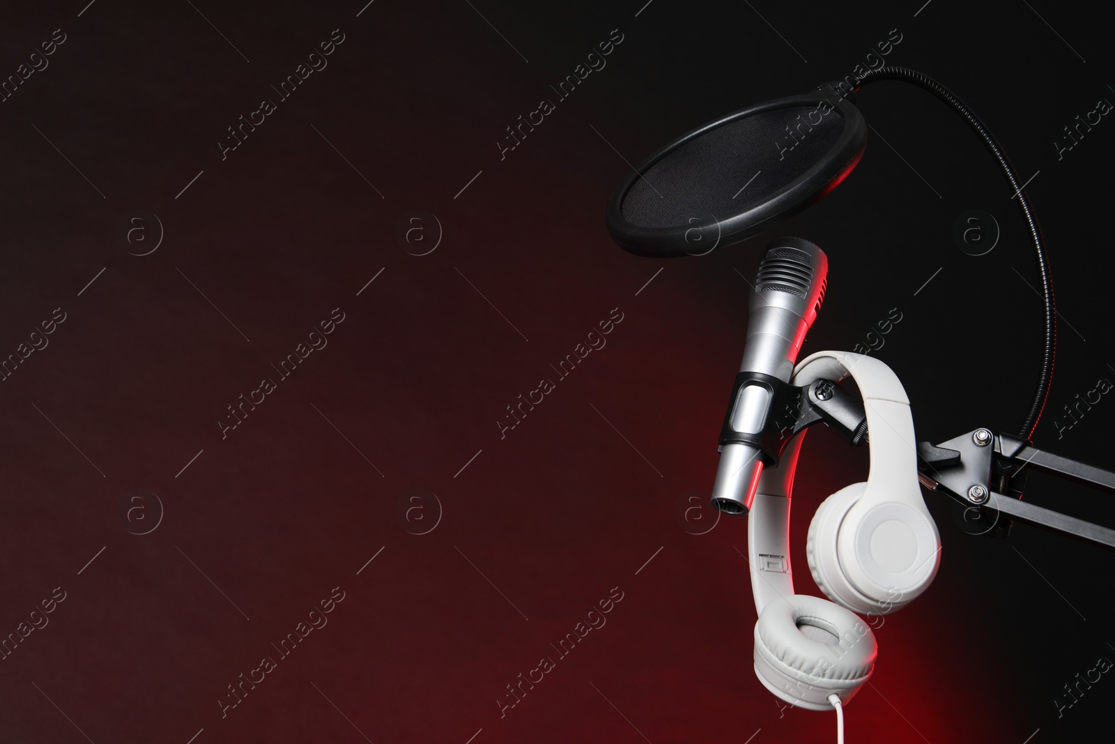 Photo of Stand with microphone, headphones and pop filter on dark background, space for text. Sound recording and reinforcement