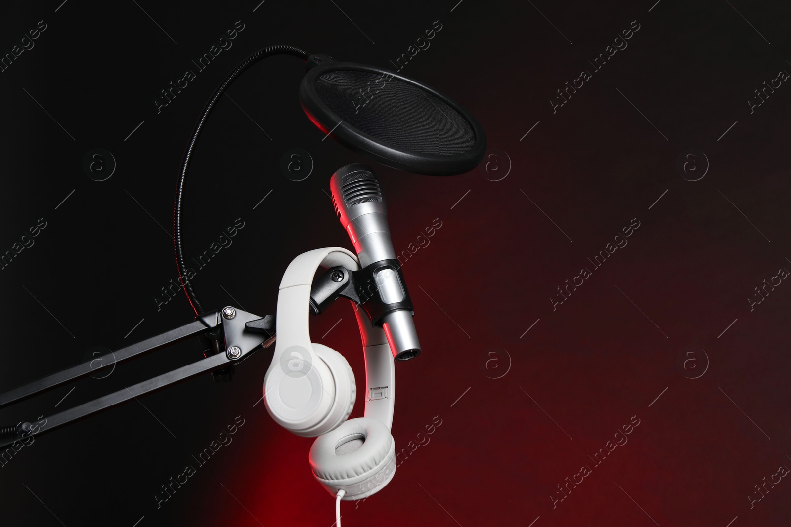 Photo of Stand with microphone, headphones and pop filter on dark background, space for text. Sound recording and reinforcement