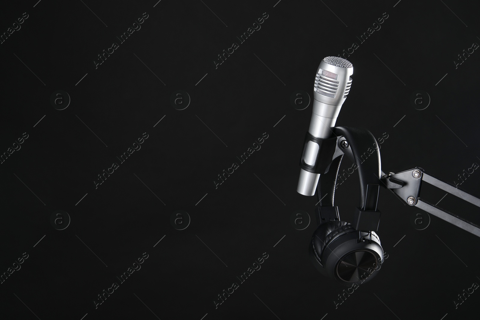 Photo of Stand with microphone and headphones on black background, space for text. Sound recording and reinforcement