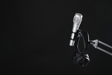 Photo of Stand with microphone and headphones on black background, space for text. Sound recording and reinforcement