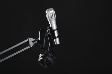 Photo of Stand with microphone and headphones on black background, space for text. Sound recording and reinforcement