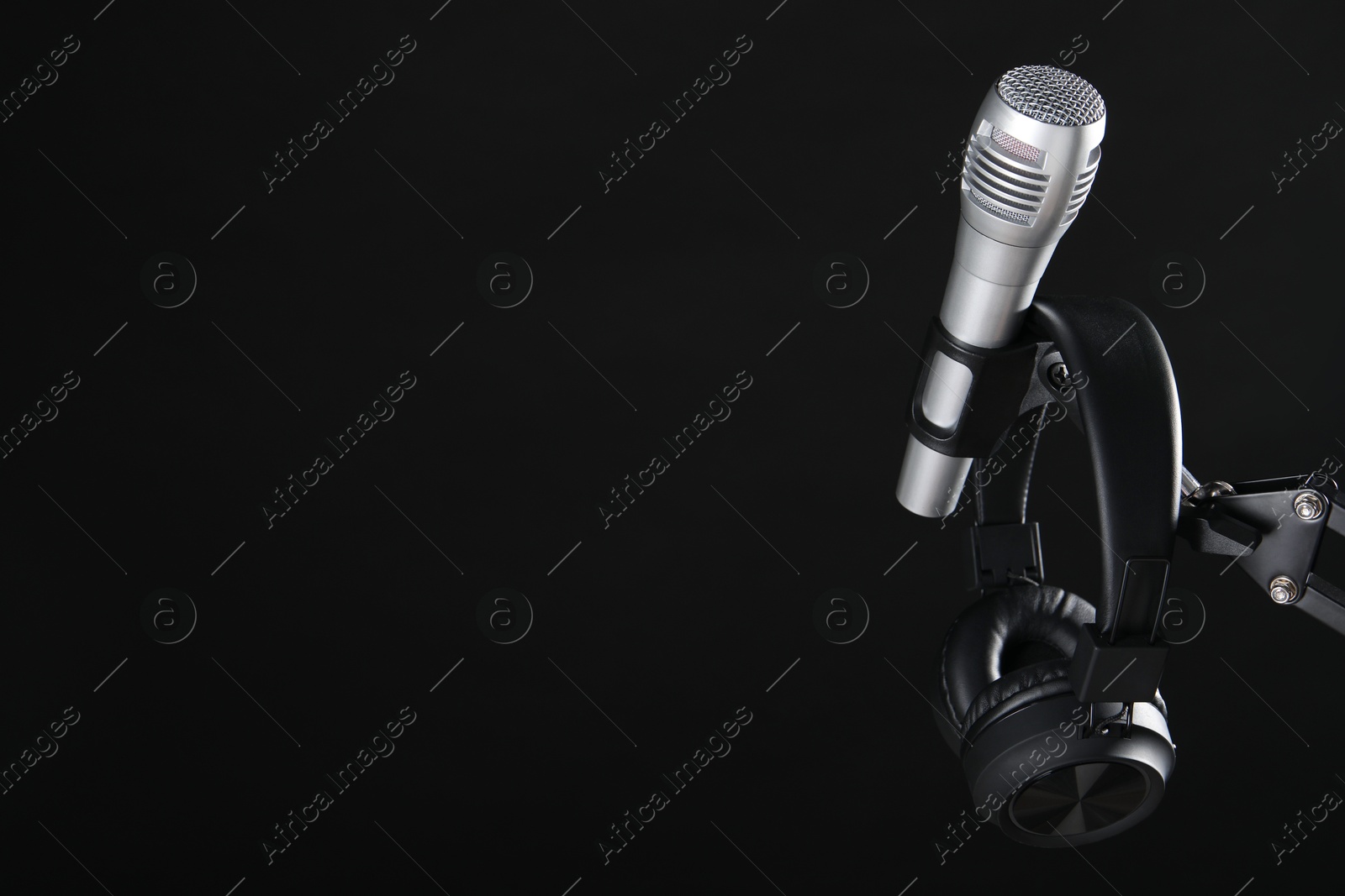 Photo of Stand with microphone and headphones on black background, space for text. Sound recording and reinforcement