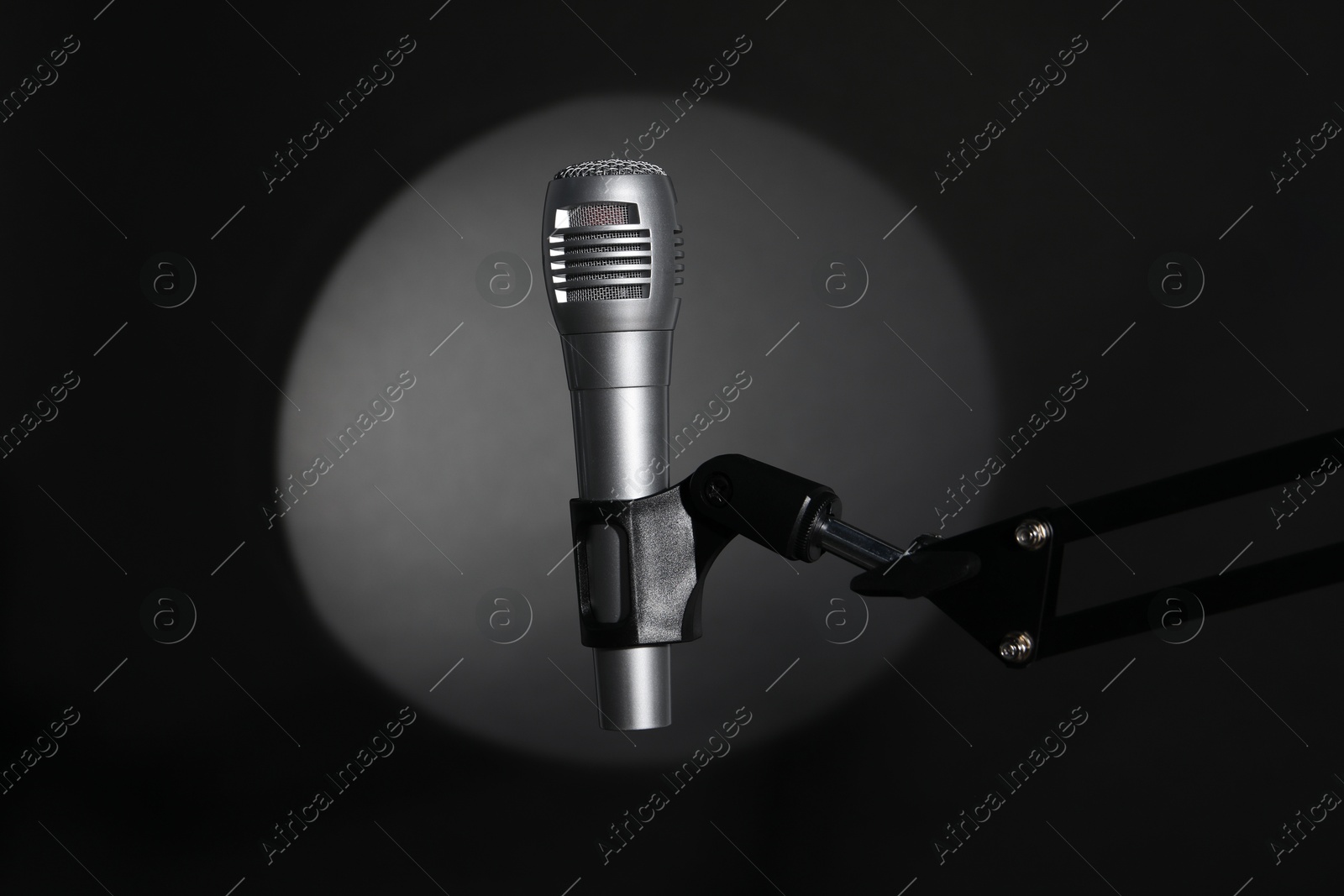 Photo of Stand with microphone in spotlight on black background. Sound recording and reinforcement