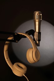 Photo of Stand with microphone and headphones in spotlight on black background. Sound recording and reinforcement