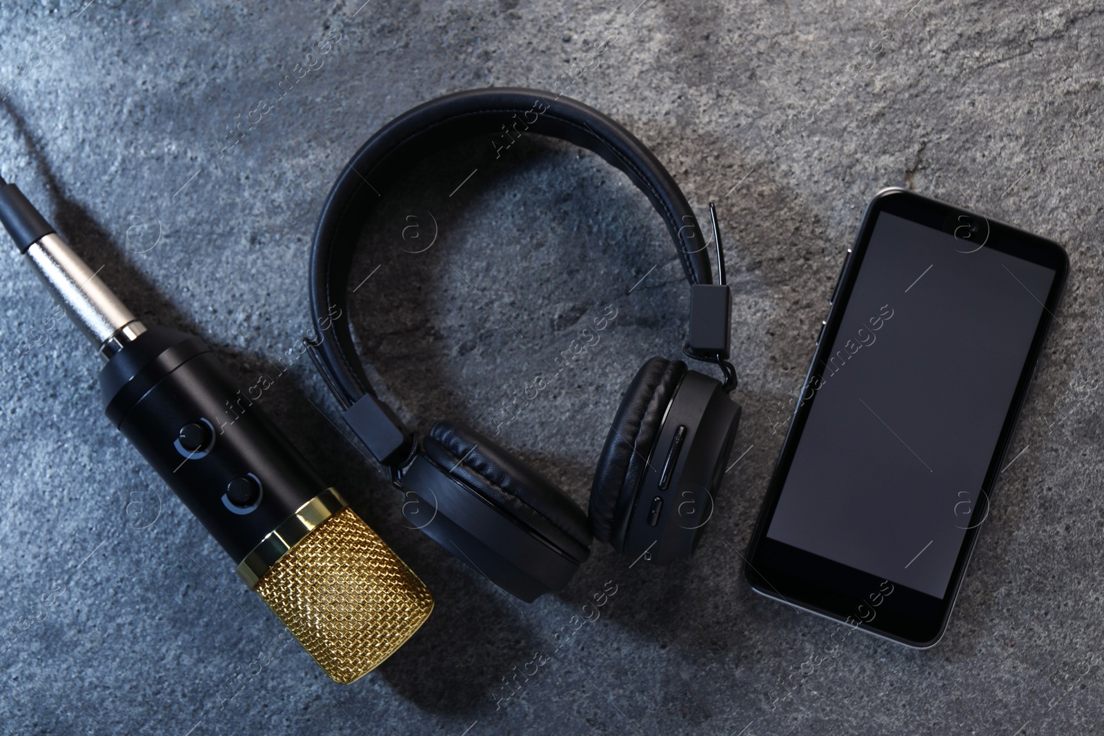 Photo of Smartphone with blank screen, headphones and microphone on grey textured background, flat lay. Sound recording and reinforcement