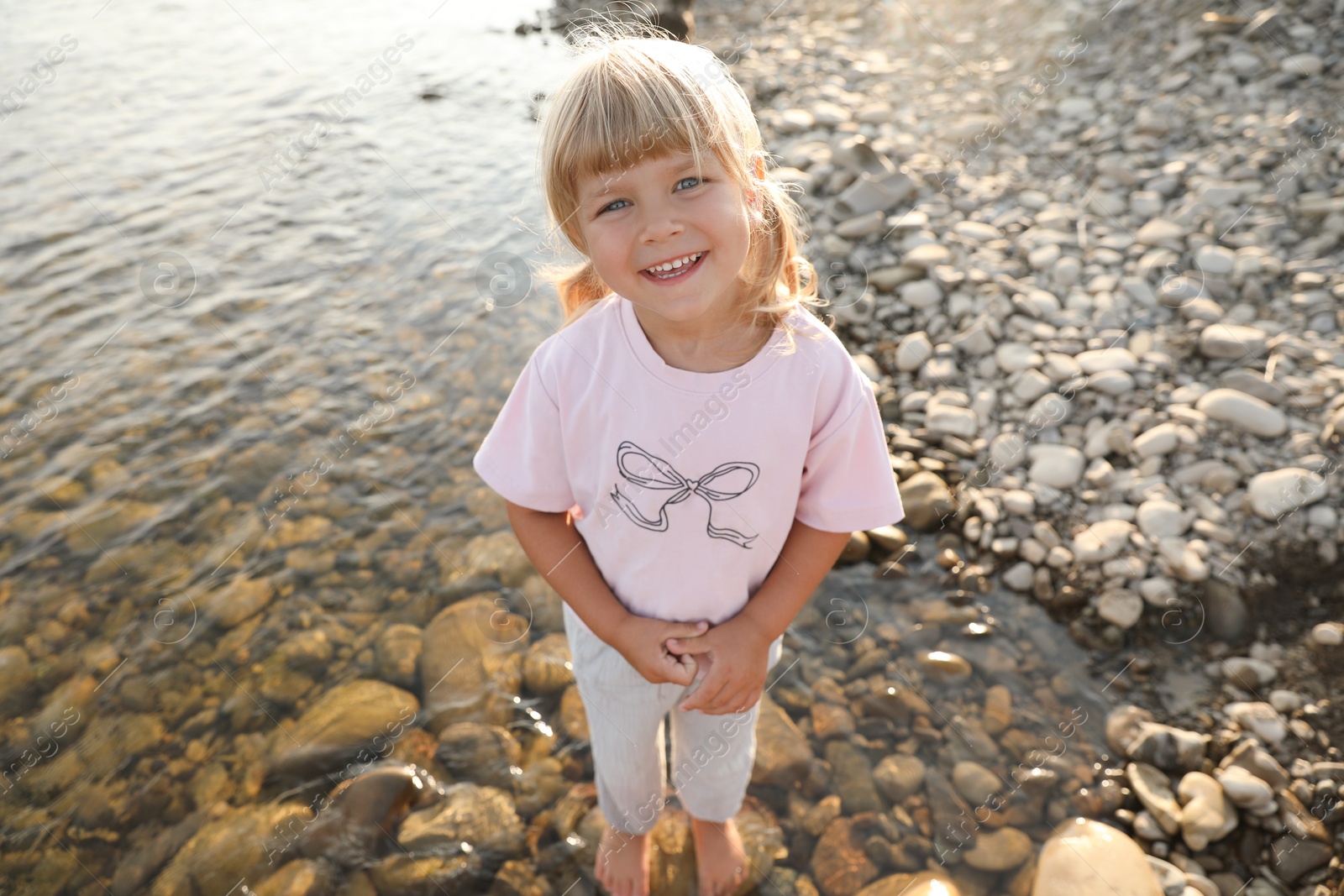 Photo of Cute little girl standing in water, above view. Child enjoying beautiful nature