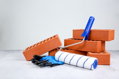 Photo of Red bricks, paint roller and gloves on textured table against light background