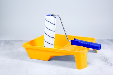 Photo of Paint roller and yellow tray on textured table against light background. Building material