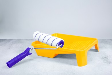 Photo of Paint roller and yellow tray on textured table against light background. Building material