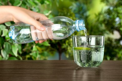 Photo of Woman pouring soda water from bottle into glass at wooden table, closeup