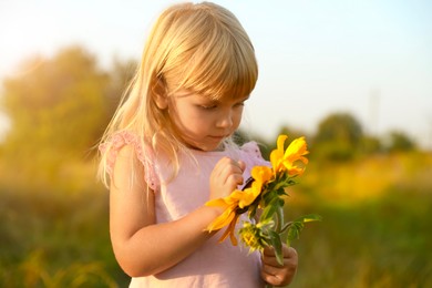 Little girl with sunflower at meadow. Child enjoying beautiful nature