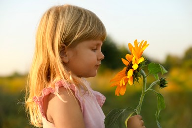 Little girl with sunflower at meadow. Child enjoying beautiful nature