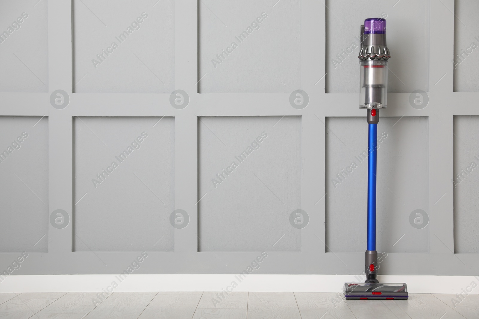 Photo of One cordless vacuum cleaner near grey wall indoors. Space for text