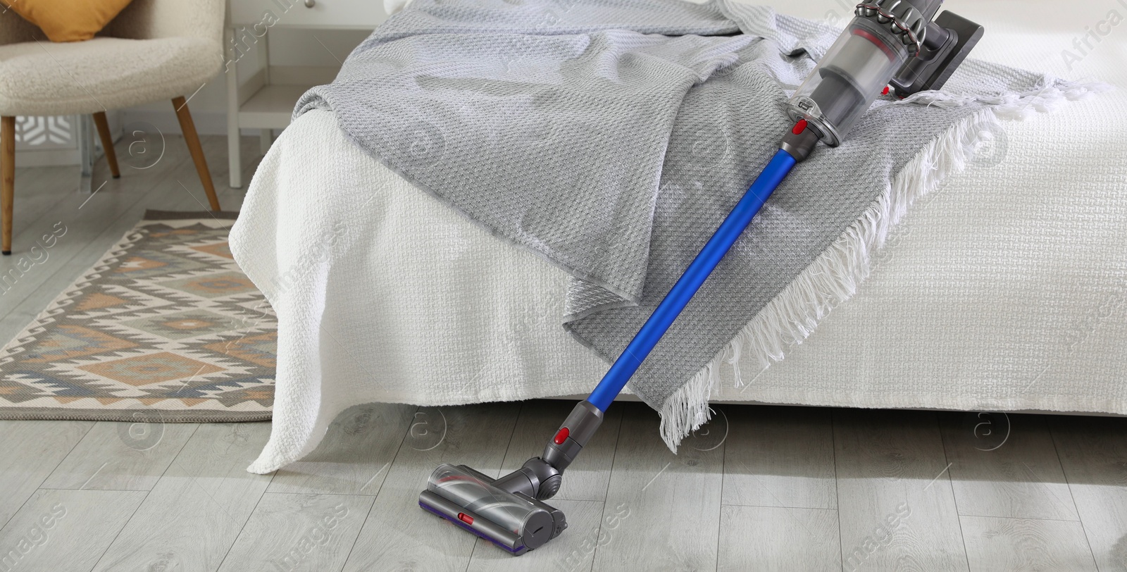 Photo of One cordless vacuum cleaner leaning on bed indoors