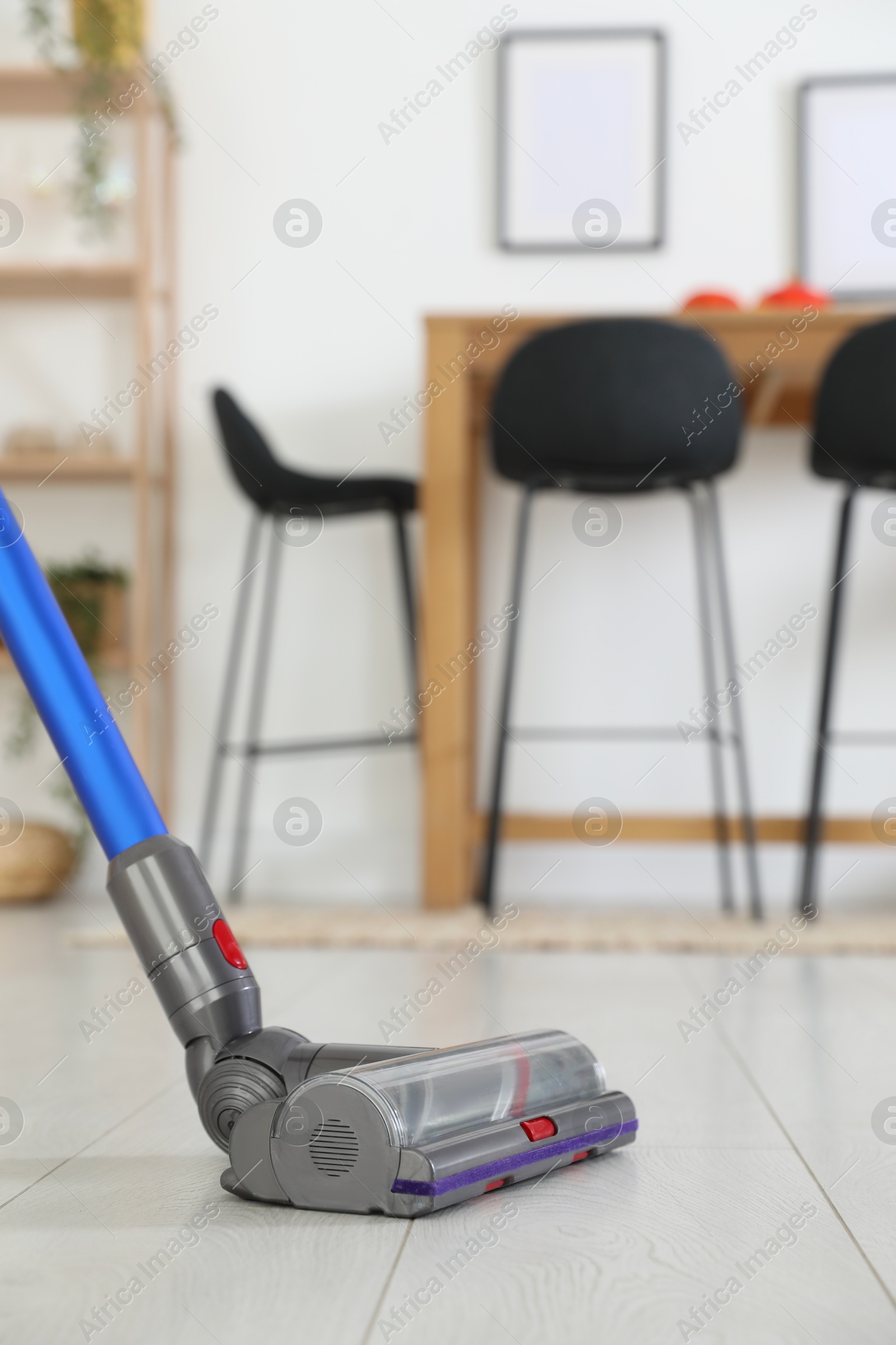 Photo of Cleaning floor with cordless vacuum cleaner indoors, closeup. Space for text