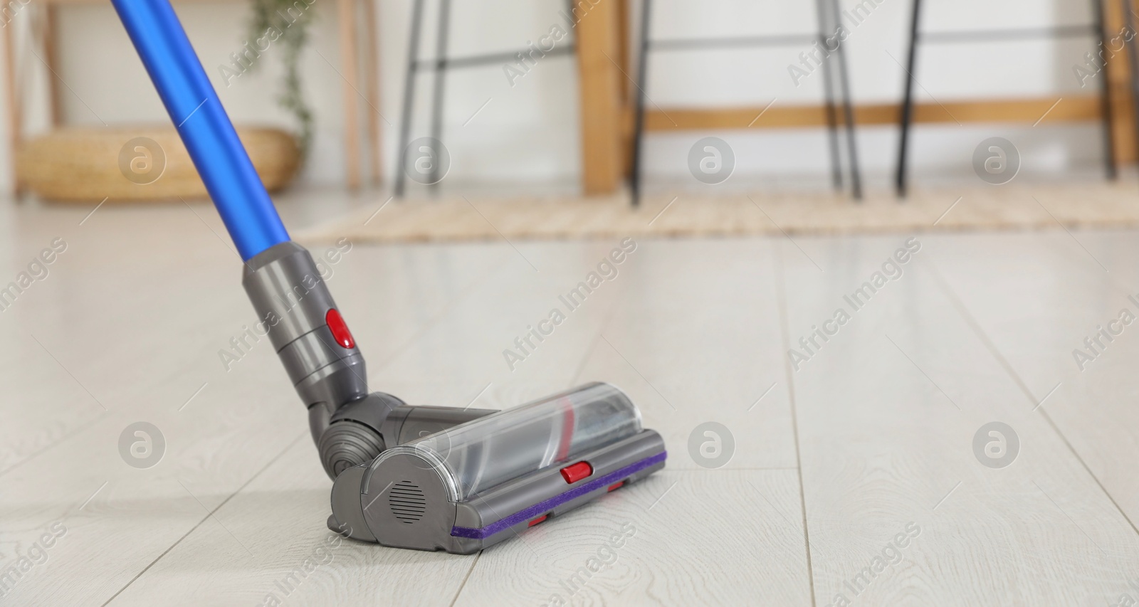 Photo of Cleaning floor with cordless vacuum cleaner indoors, closeup. Space for text