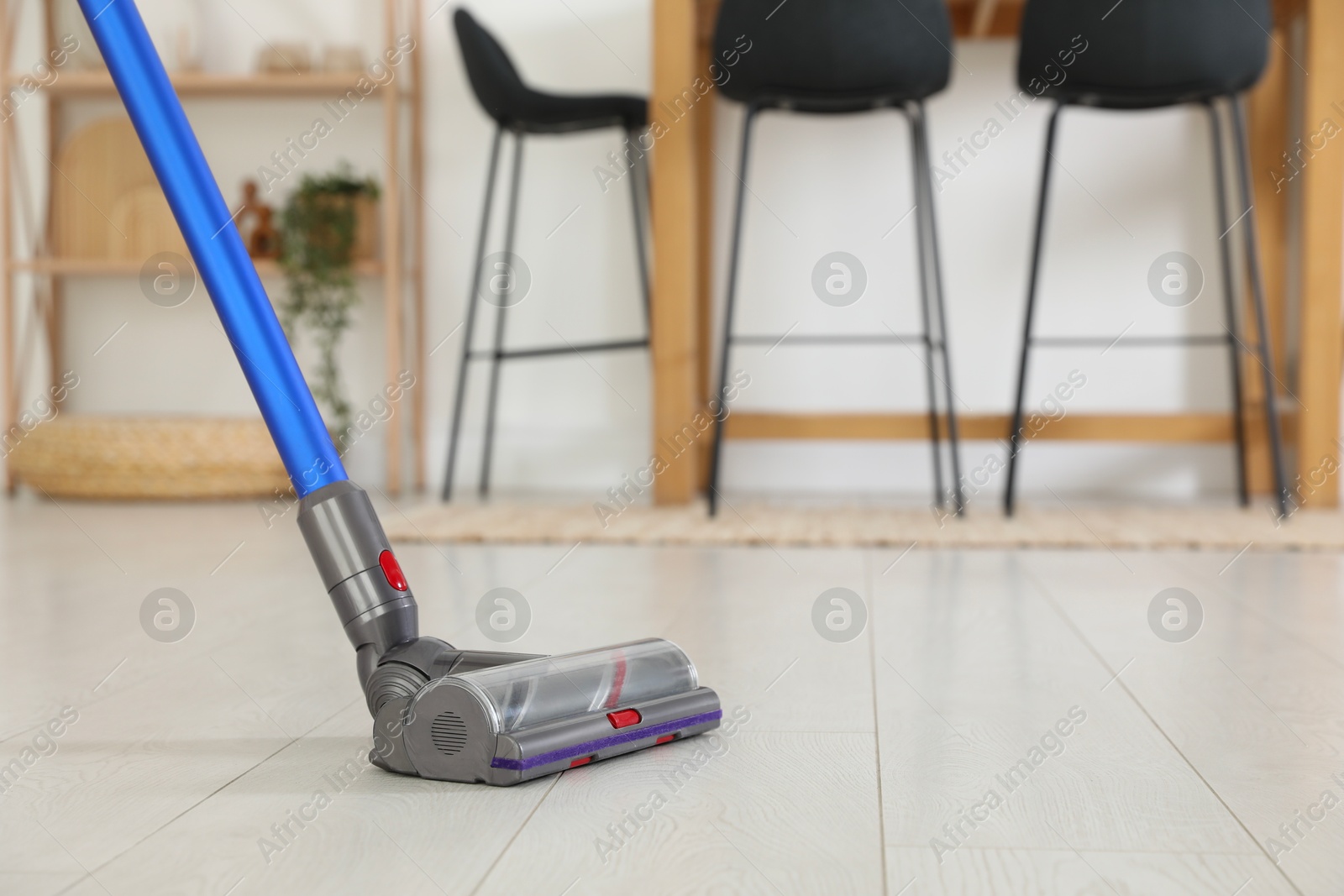 Photo of Cleaning floor with cordless vacuum cleaner indoors, closeup. Space for text