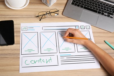 Photo of Developing UI design. Designer with smartphone creating website wireframe on paper at wooden table, closeup