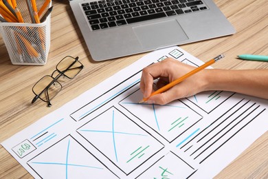 Photo of Developing UI design. Designer with smartphone creating website wireframe on paper at wooden table, closeup