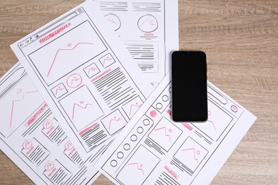 Photo of Developing UI design. Sketches of website wireframes and smartphone on wooden table, top view