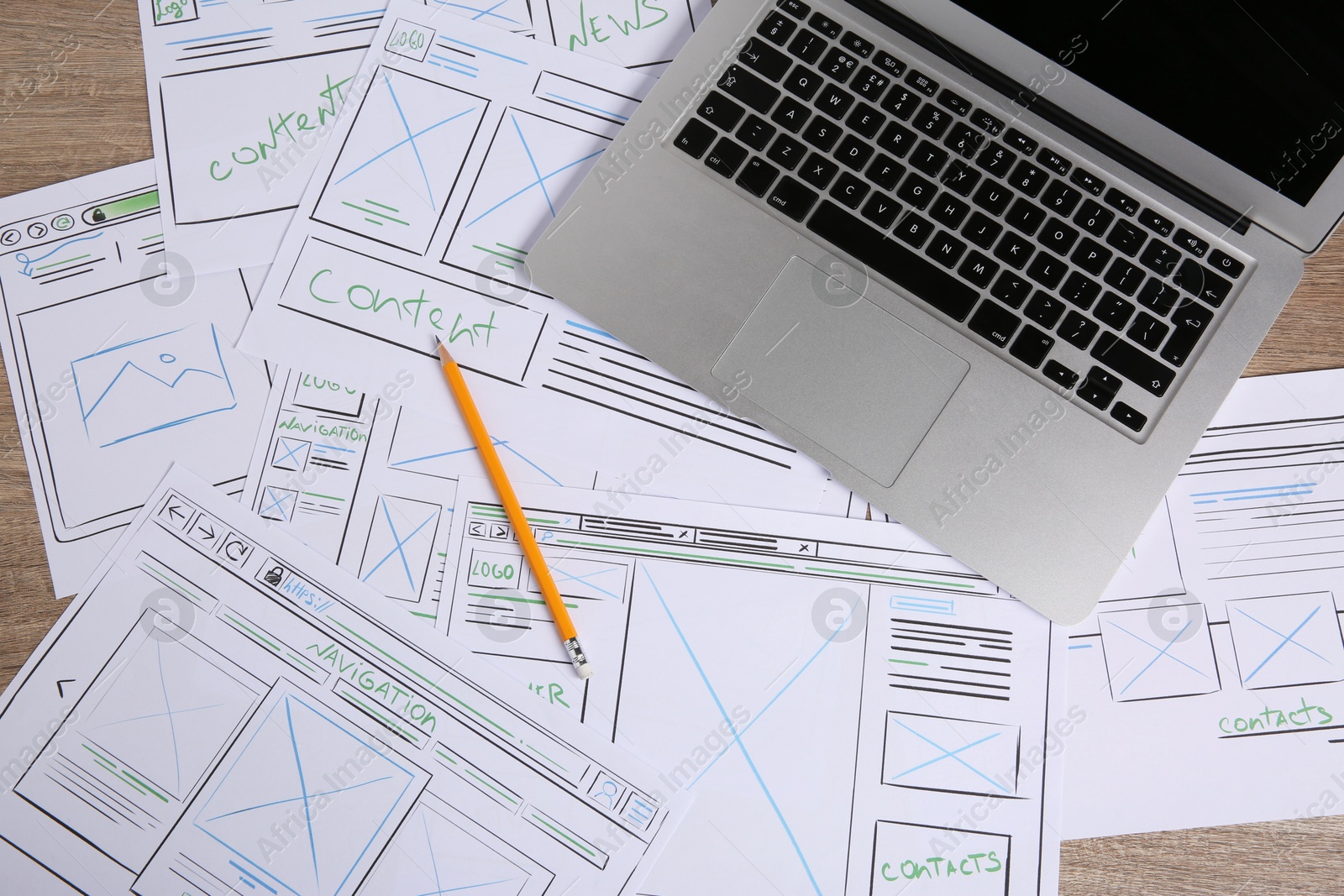 Photo of Developing UI design. Sketches of website wireframes, laptop and pencil on wooden table, top view