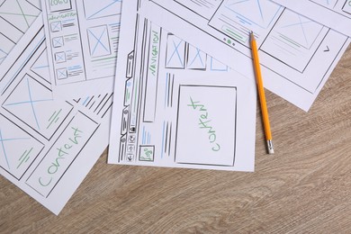 Developing UI design. Sketches of website wireframes and pencil on wooden table, top view