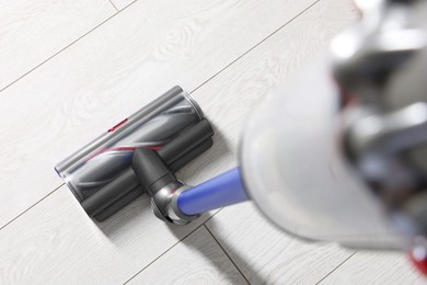 Photo of Cleaning floor with cordless vacuum cleaner indoors, closeup