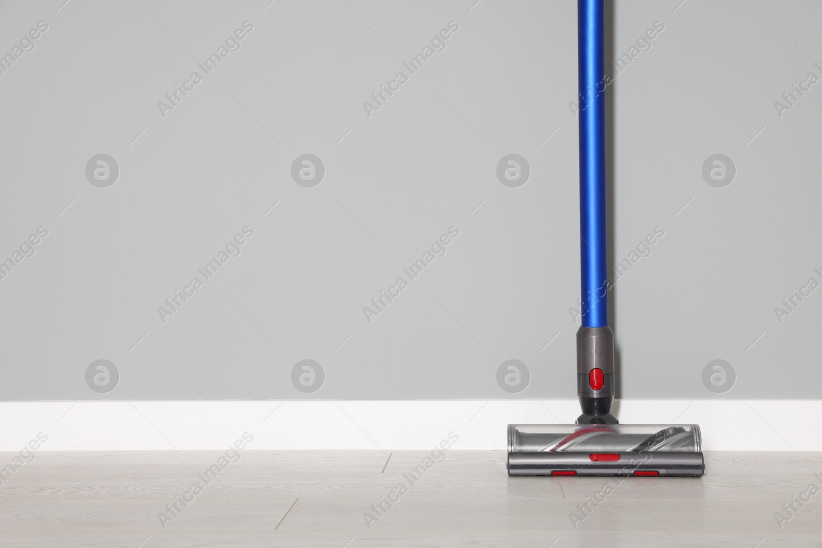 Photo of One cordless vacuum cleaner near grey wall indoors. Space for text