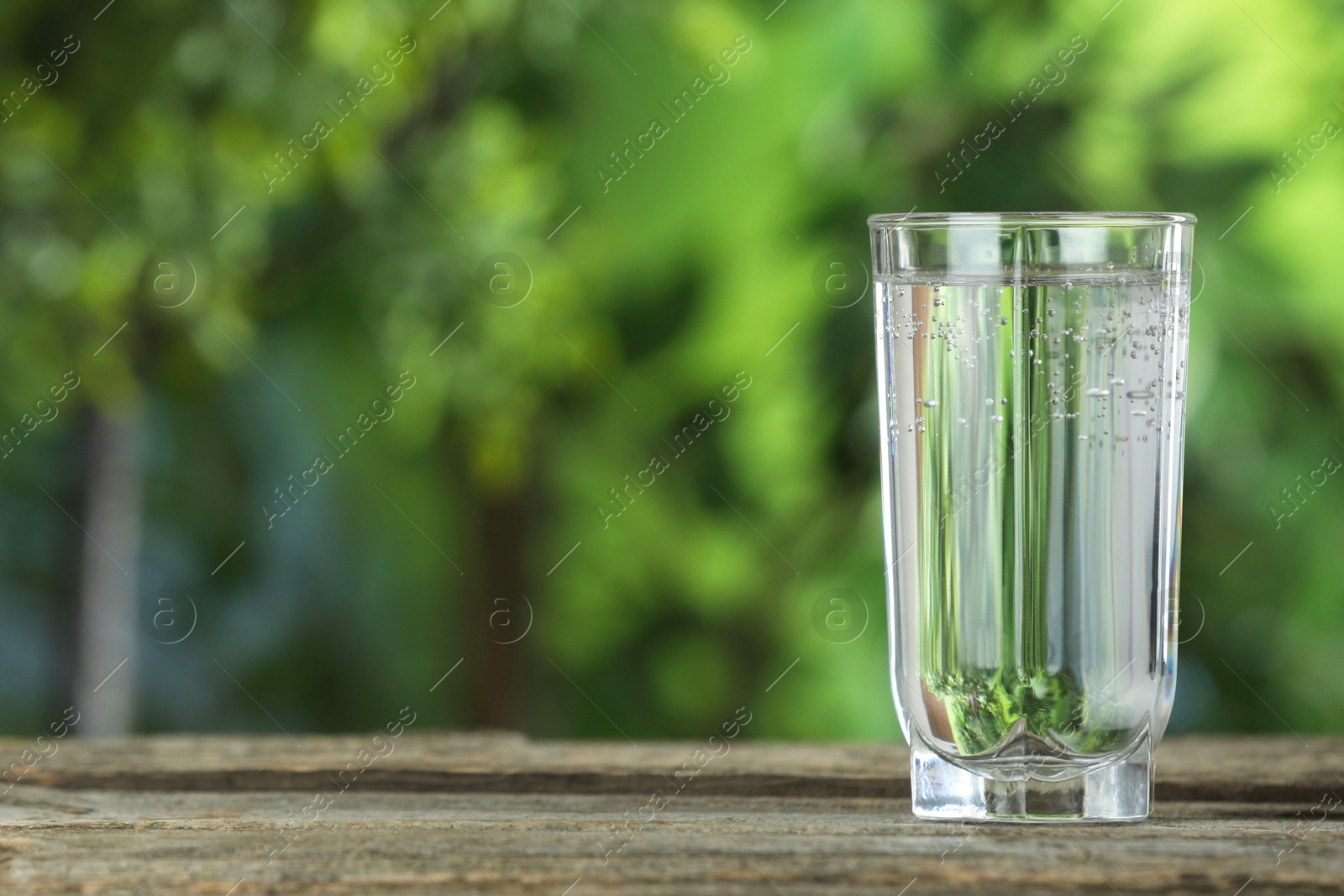 Photo of Soda water in glass on wooden table outdoors, space for text