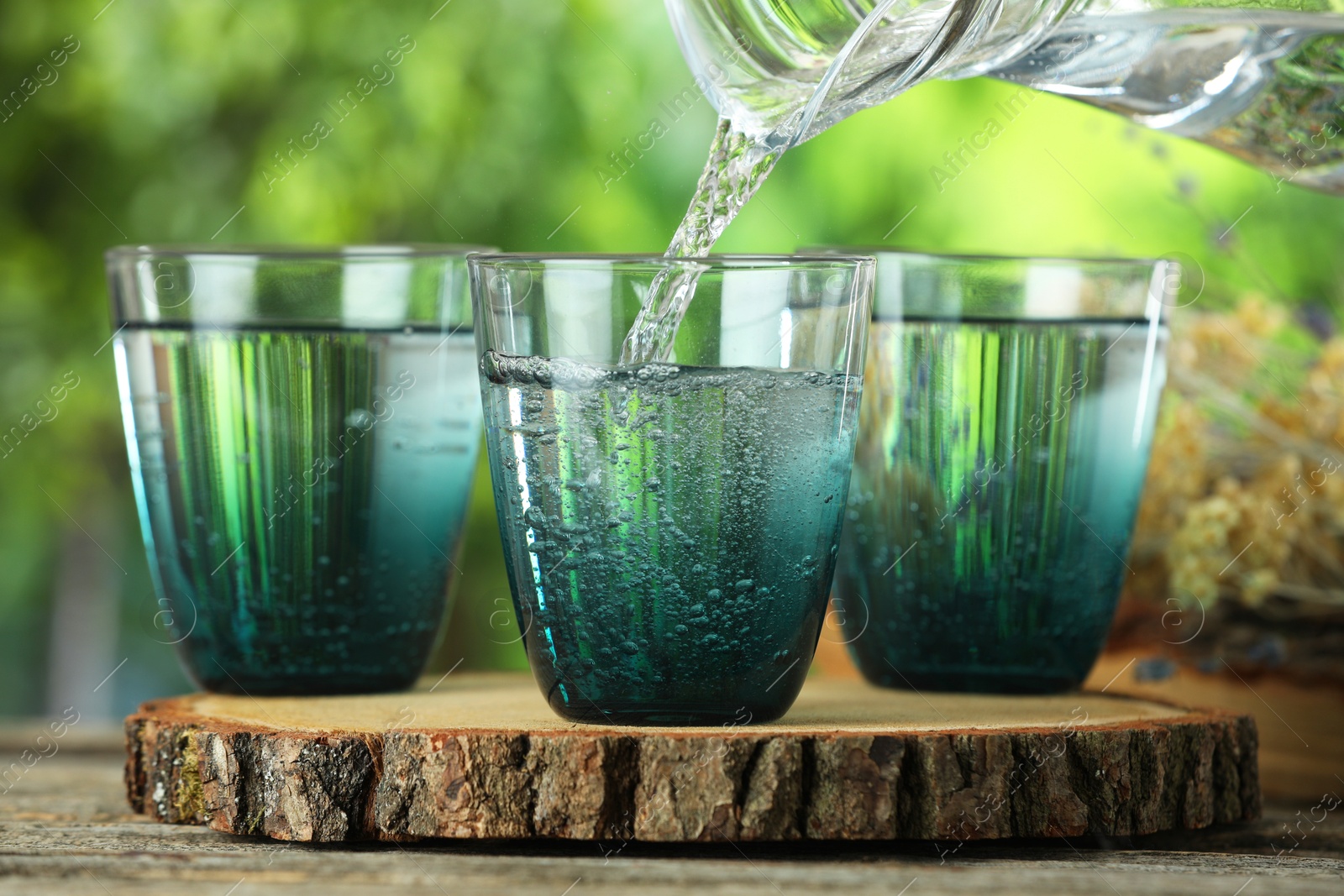 Photo of Pouring soda water in glass at wooden table outdoors