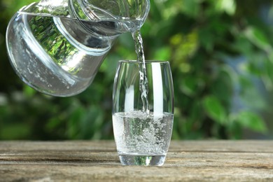 Photo of Pouring soda water in glass at wooden table outdoors