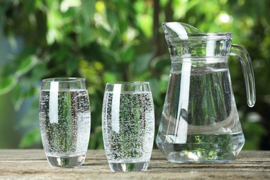 Photo of Soda water in glasses and jug on wooden table outdoors