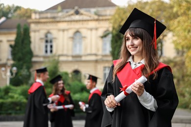 Photo of Happy students with diplomas after graduation ceremony outdoors, selective focus