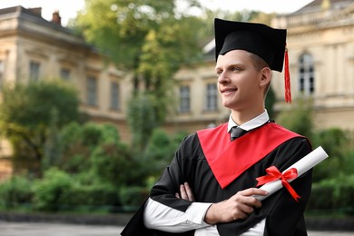 Happy student with diploma after graduation ceremony outdoors, space for text