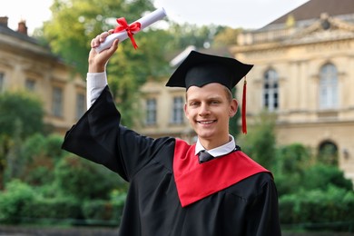 Photo of Happy student with diploma after graduation ceremony outdoors